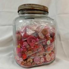 The image displays a Clear glass jar filled with a collection of assorted buttons, predominantly in