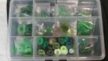Clear plastic storage container filled with various shades and styles of green buttons