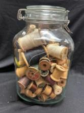 vintage Crown canning jar filled with a collection of old wooden spools of thread