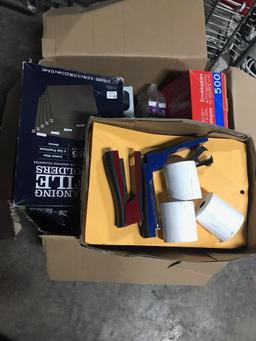 Box of office supplies including staplers, hole punch, file holders, tape, calculators