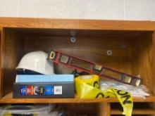 What contains items on shelves which include hardhat, caution, tape, level, three ring, binders, and