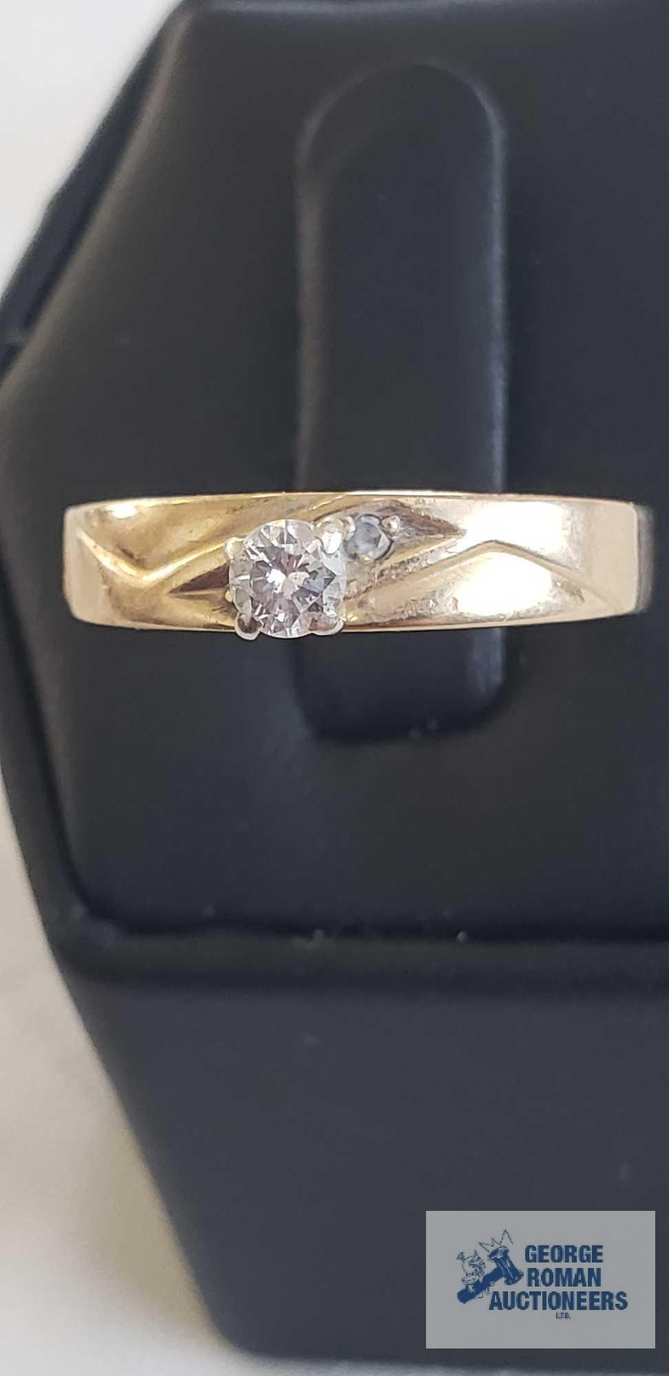 Gold colored band engagement like ring with clear gemstone and two smaller gemstones, marked Magic