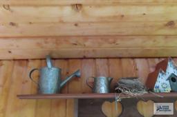 Lot of decorative watering cans, bear welcome sign and birdhouse