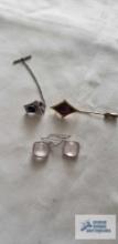Gold colored pin with purple stone, silver colored tie clip with blue stone, and pale pink earrings