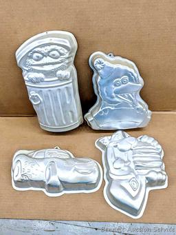 Four Wilton character cake pans including Oscar the Grouch, Cars, Scooby Doo, and Big Bird. Largest