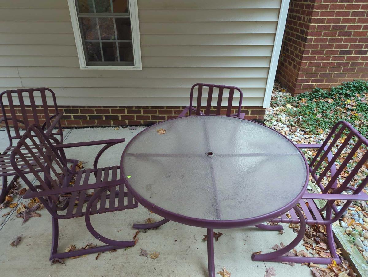 (BACK) DARK PURPLE PATIO SET WITH ROUND GLASS TOP TABLE AND 4 ARM CHAIRS. TABLE MEASURES APPROX 48"