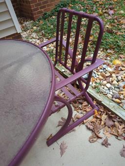 (BACK) DARK PURPLE PATIO SET WITH ROUND GLASS TOP TABLE AND 4 ARM CHAIRS. TABLE MEASURES APPROX 48"