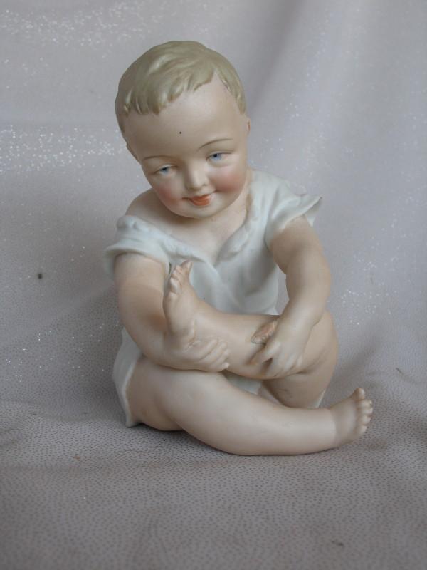 Three Figurines:- Bisque Heubach type 15cm seated boy with crossed legs inc