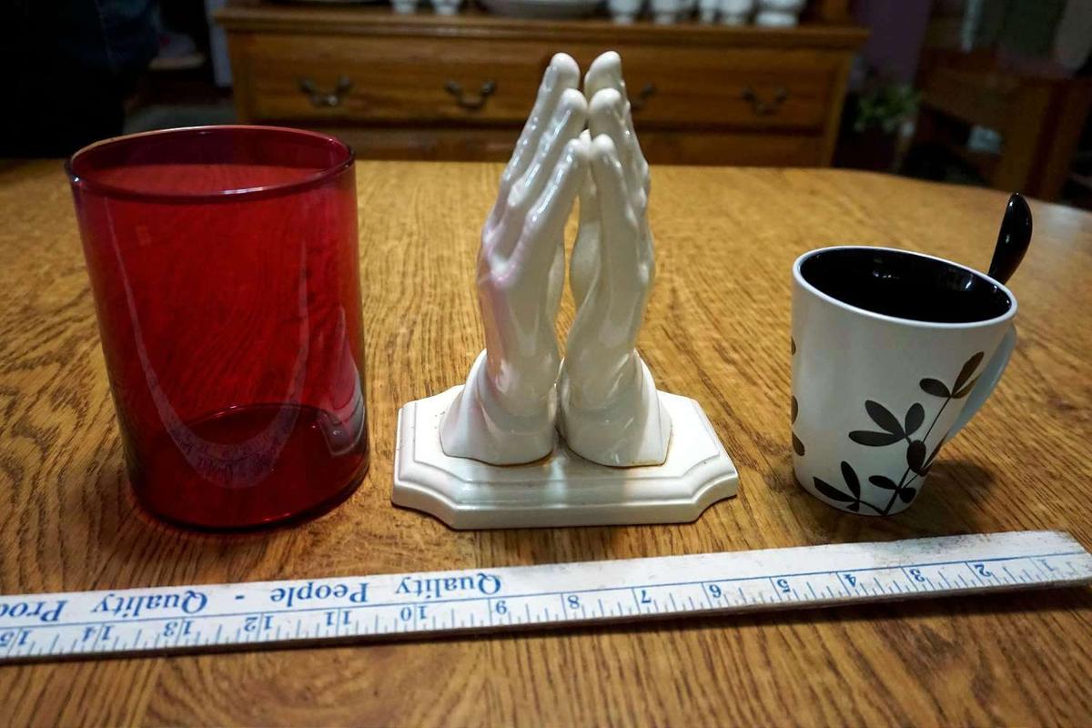 Red glass, coffee mug with spoon, praying hands.