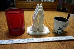Red glass, coffee mug with spoon, praying hands.