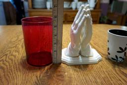 Red glass, coffee mug with spoon, praying hands.