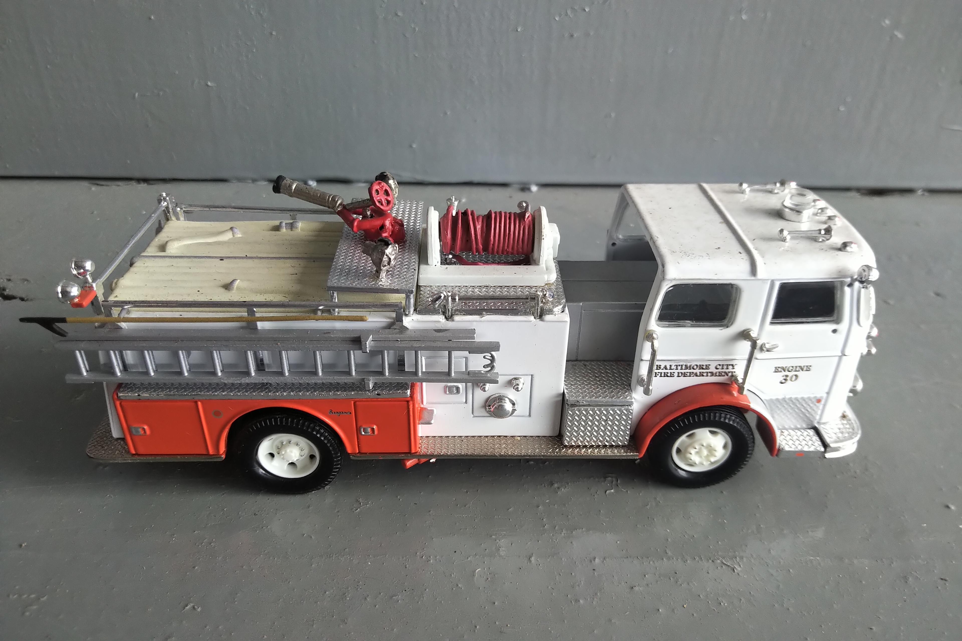 A TUBE OF 12 - 1/64 SCALE FIRE TRUCKS, A 1/64 SCALE POLICE CAR