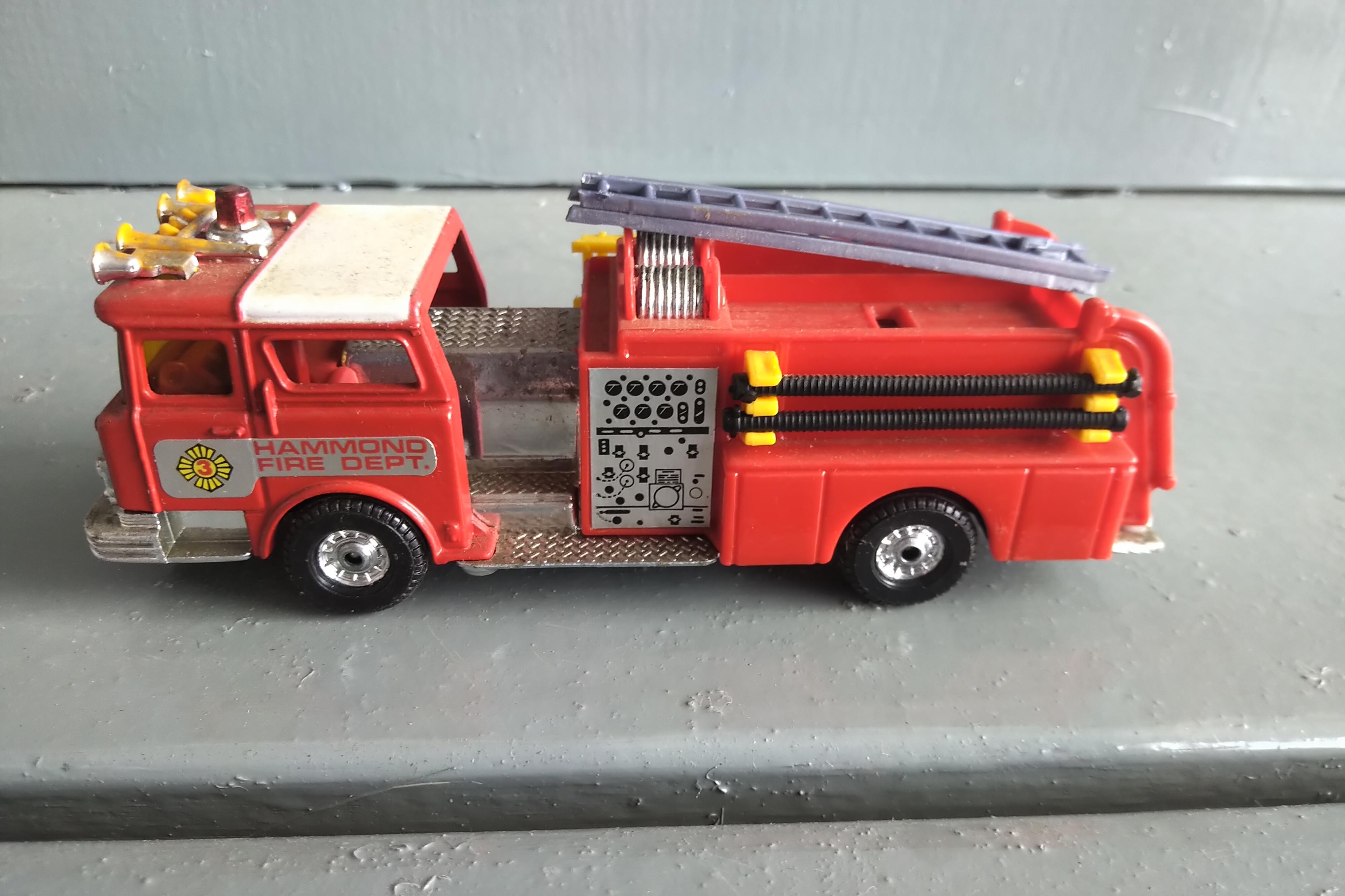 A TUBE OF 12 - 1/64 SCALE FIRE TRUCKS, A 1/64 SCALE POLICE CAR