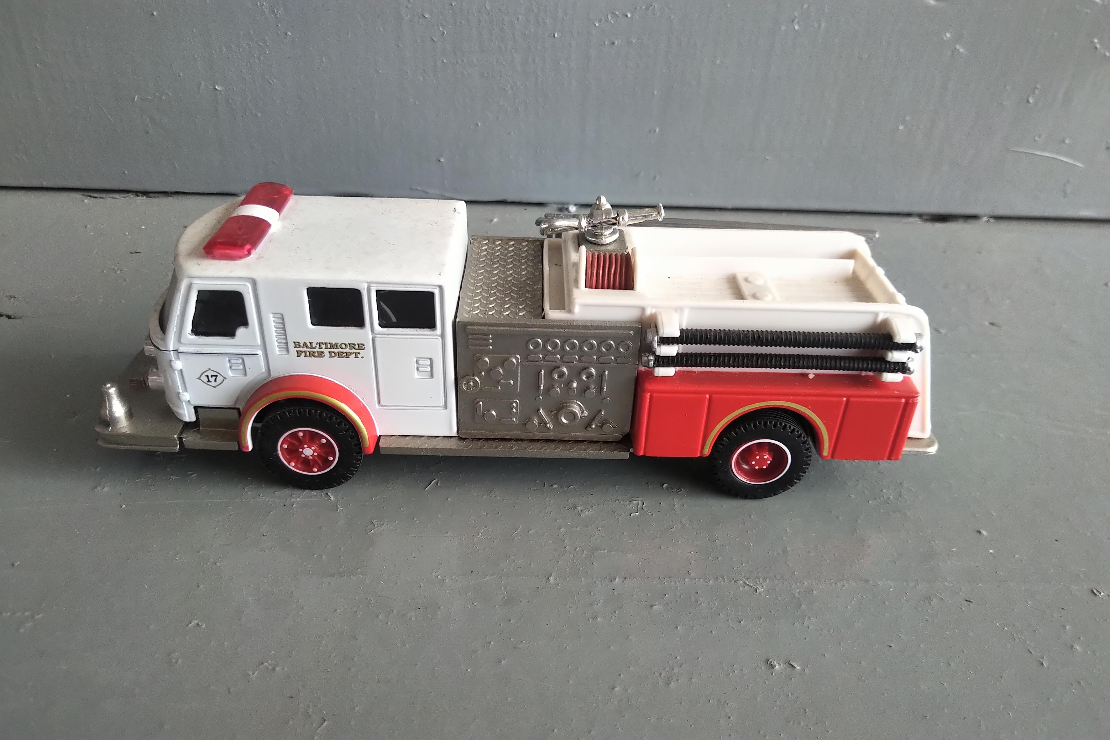 A TUBE OF 12 - 1/64 SCALE FIRE TRUCKS, A 1/64 SCALE POLICE CAR