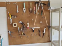 mixed yard and mechanics tools with peg hooks on peg board