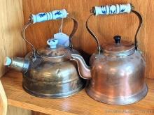 Two copper colored tea kettles with ceramic or similar handles. Taller measures nearly 10" over