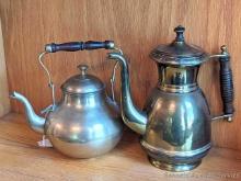 Set of 2 brass or similar colored hot water or tea kettles. Both feature a wooden handle and covers.