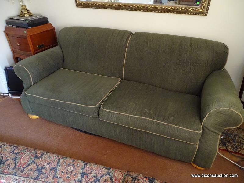 (LR) GREEN 2 CUSHION SOFA. HAS BUN FEET AND TRIMMED WITH TAN PIPING. 88"X44"X36". GOOD USED