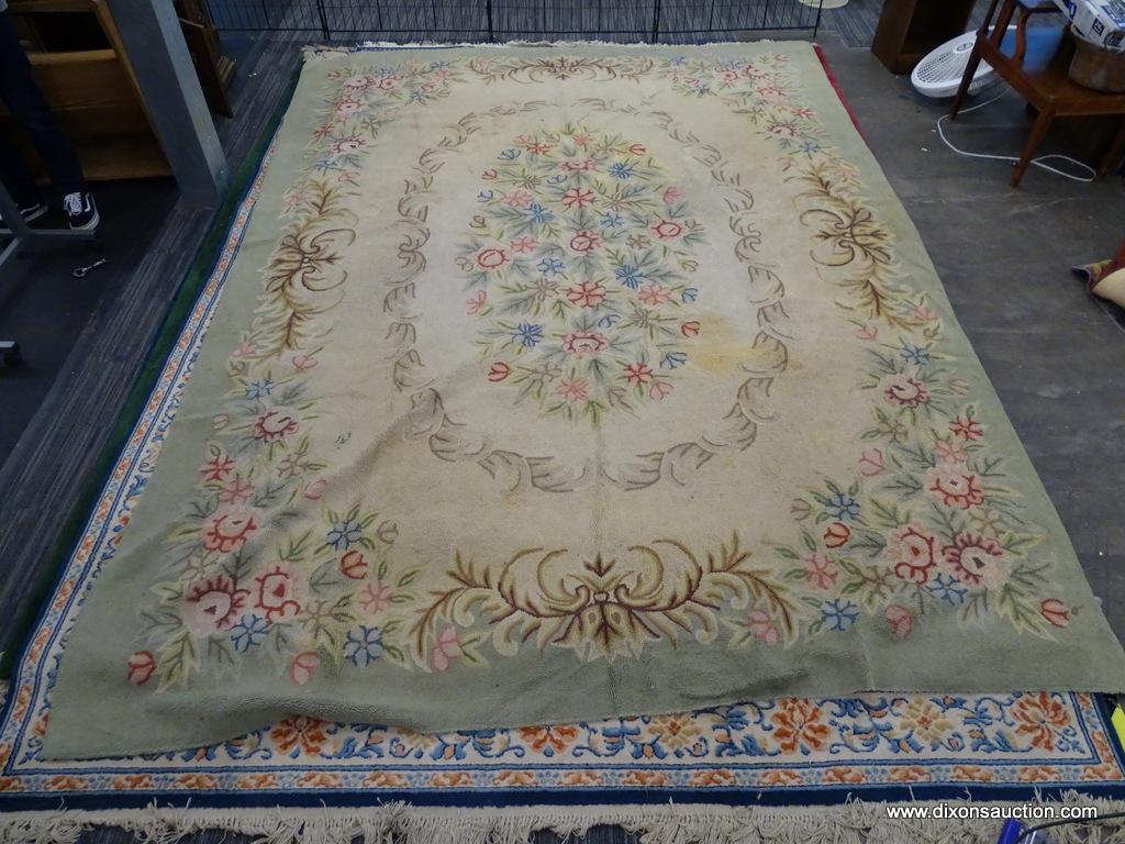 WOVEN AREA RUG; HAS A BEIGE AND GREEN COLOR BASE WITH PINK AND BLUE FLOWERS. HAS BROWN COLORED