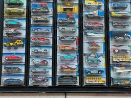 (LOCATED CENTER AISLE) HOT WHEELS CARS IN ORIGINAL PACKAGES IN BLACK DISPLAY RACK. MOSTLY 1990S