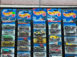 (LOCATED CENTER AISLE) HOT WHEELS CARS IN ORIGINAL PACKAGES IN BLACK DISPLAY RACK. MOSTLY 1990S