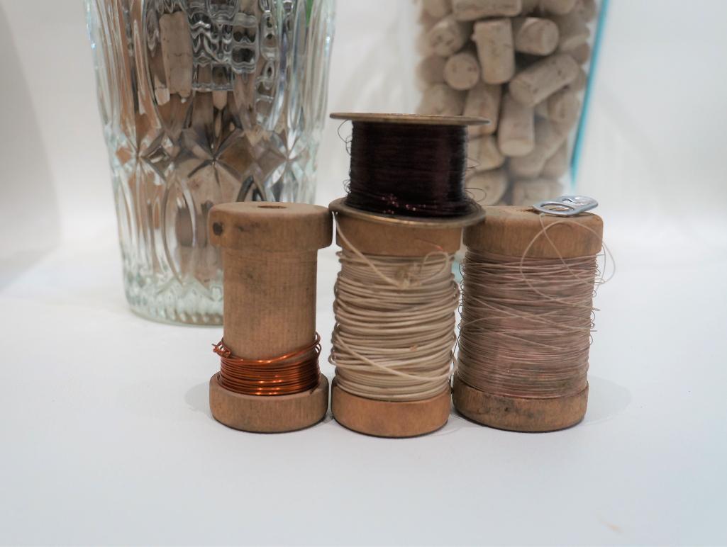 (12L) TWO TALL TAPERED GLASS VASES FILLED WITH CRAFTS SUPPLY ITEMS: CORKS, PULL TABS, WOODEN SPOOLS,