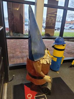 BENCHMADE METAL GNOME YARD ORNAMENT. HE IS WEARING A BLUE HAT AND A RED OUTFIT. MEASURES APPROX 25"