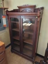 (LAU) ANTIQUE WOOD GLASS FRONT BOOKCASE FEATURING REEDED SIDES, CARVED DETAILED BACK SPLASH TOP. THE