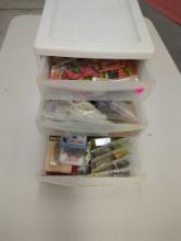 White three drawer organizer filled with unopened fishing lures and other accessories. Comes as is